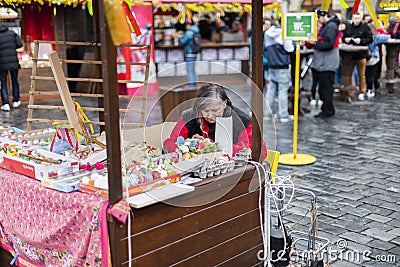 MARCH 25, 2016: An older lady selling decorated eggs in her wooden booth at the Easter markets on Old Towns Square, Prague Editorial Stock Photo