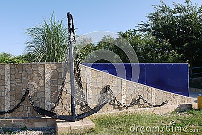 Marine anchor with a chain painted in black paint. Standing in the park leaned against a low wall made of stone. Stock Photo