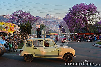Market day in Antananarivo, a vintage renault taxi drives near jacaranda trees blossoming Editorial Stock Photo