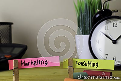 Marketing and Consulting. Handwriting on sticky notes in clothes pegs on wooden office desk Stock Photo