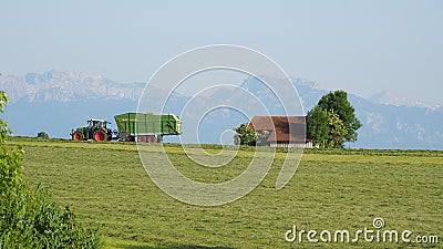 Marktoberdorf, Germany. Green fields with grass and hay cut ready to be harvested. Fendt tractor with hay collection Tigo trailer Editorial Stock Photo