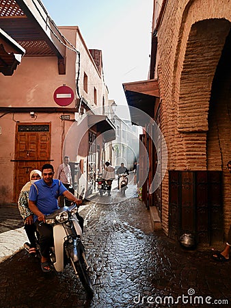 Marrakech, Morocco, 24.10.2021. Moroccan couple riding motorbike in Medina. Ray of sun in narrow alleyway. Editorial Stock Photo