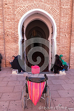 Marrakesh, Morocco - March 13, 2018: A man in a wheelchair waits at the entrance of the Koutoubia Mosque for someone to help him Editorial Stock Photo