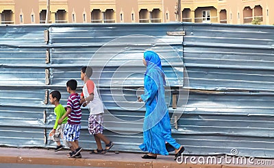 Veiled Muslim woman with three children in front of corrugated metal fence at construction site Editorial Stock Photo