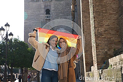 Marriage of lesbians on holiday and tourism in sevilla. They are in front of the cathedral and hold the gay pride flag in their Stock Photo