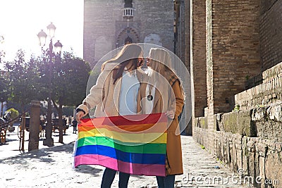 Marriage of lesbians on holiday and tourism in seville. They are in front of the cathedral and they are holding the gay pride flag Stock Photo
