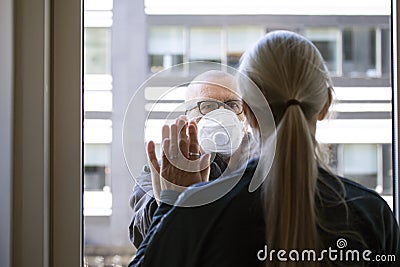 A married couple separated by Corona Covid-19 virus. She is quarantined indoors and he is outside wearing protective mask. They ar Stock Photo