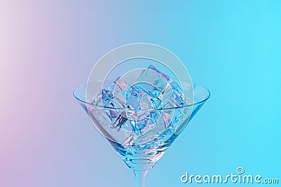 Martini glass with ice cubes in neon holographic vibrant pink and blue colors. Minimal celebration concept Stock Photo