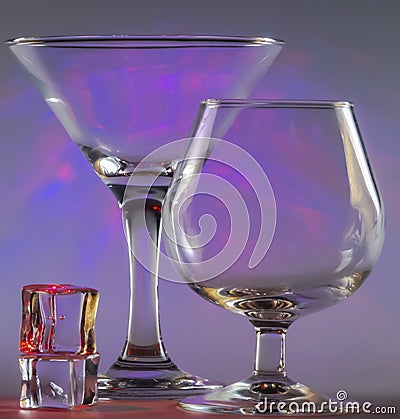 Martini Glass together with Cognac Glass and ice cubes with flashing smooth violet lights on background Stock Photo