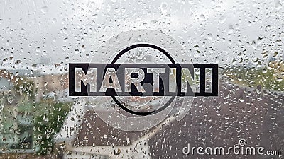 Martini sticker logo. A brand of Italian-made vermouths and sparkling wines. Water drop on glass window during rain with blurred Editorial Stock Photo