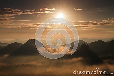 Marvelous daybreak. Autumn sunset view over forest to fall colorful valley full of dense mist colred with hot sun rays Stock Photo