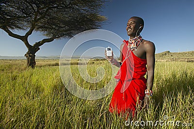 Masai Warrior near Acacia Tree listening to music on iPod by Apple in red surveying landscape of Lewa Conservancy, Kenya Africa Editorial Stock Photo