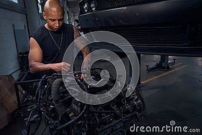 Masculine African American auto-mechanic standing near big black engine Stock Photo