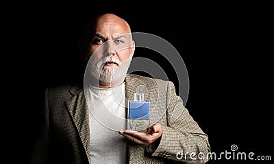 Masculine perfume, bearded old man in suit. Male holding up bottle of perfume. Aged man perfume, fragrance. Perfume or Stock Photo