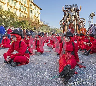 Masked figures sitting on the street with the allegorical float `Idol` in the background, Carnival of Viareggio, Italy Editorial Stock Photo