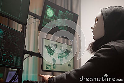 Masked hacker with a hoodie using computer to plan a massive cyber attack Stock Photo