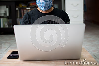 The masked man sat on the floor and worked at home using a laptop and holding a smartphone on a wooden table during the Stock Photo