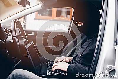 Masked thief hacker in a balaclava disarming car security systems Stock Photo