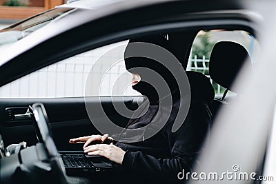 Masked thief hacker in a balaclava disarming car security systems Stock Photo