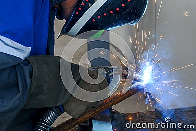 Masked welder works in workshop and sparks fly. Close-up portrait. Industrial background. Authentic workflow. Stock Photo