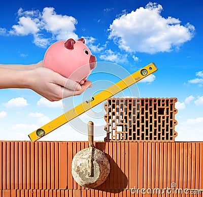 Masonry tools on a brick wall and a hand holding a piggy bank Stock Photo