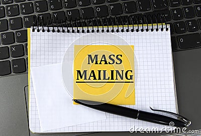 MASS MAILING - words on a yellow piece of paper on the background of a laptop with a notebook and a pen Stock Photo
