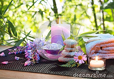 Massage in the bamboo garden with violet flowers, candles and towel Stock Photo