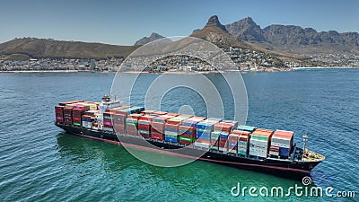 Massive cargo vessel traveling through water in front of a majestic mountain backdrop Editorial Stock Photo