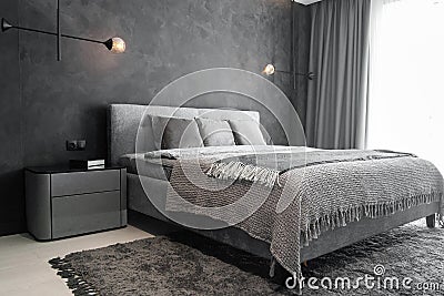 Master bedroom for a lonely stylish man, a bachelor. Modern room with trendy gray interiors, large king-size and lamps. Stock Photo