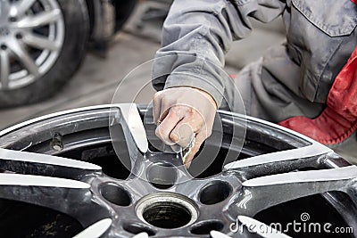 Master body repair man is working on preparing the surface of the aluminum wheel of the car for subsequent painting in the Stock Photo
