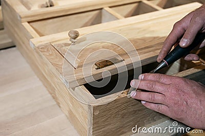 master carpenter works with a hand tool with a chisel, sets the hinges on the cabinet. Production of handmade wooden furniture. Stock Photo