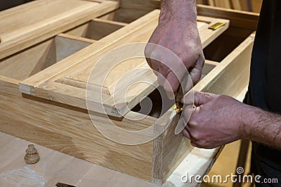master carpenter works with a hand tool, sets the hinges on the cabinet. Production of handmade wooden furniture. Stock Photo