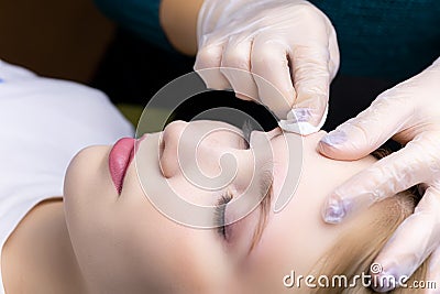 The master erases excess eyebrow styling with a cotton swab from the model`s face Stock Photo