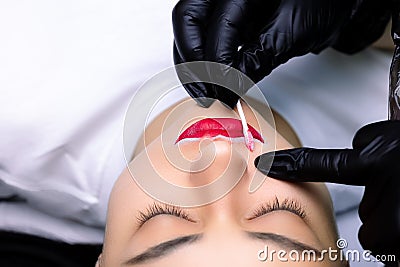 The master erases the remnants of the pigment applied to the lips with a cotton swab Stock Photo