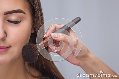 Master inflicts brush powder on the face of the girl, completes the day make-up in a beauty salon. Stock Photo