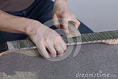 The master polishes the frets on the fretboard of the guitar. The fingerboard is protected by molar tape Stock Photo