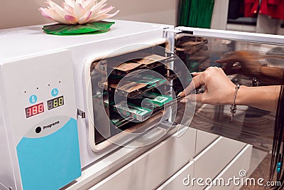 The master puts the manicure tools into the sterilizer. Sterilization of instruments in a beauty salon. Sterilization. Equipment Editorial Stock Photo