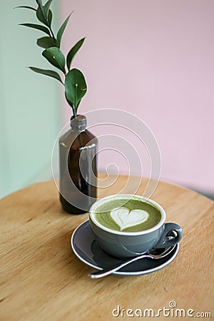 Matcha Latte heart shaped art in a grey cup on a brown table with pastel background Stock Photo