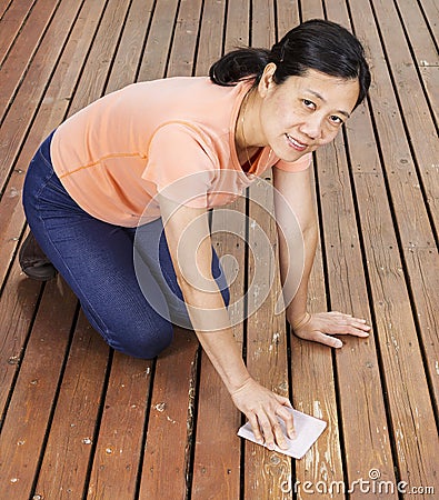 Matue woman sanding natural cedar wooden deck by hand Stock Photo