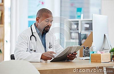 Mature african american doctor checking a patients chart. Focused gp reading a chart on a clipboard. Serious doctor Stock Photo