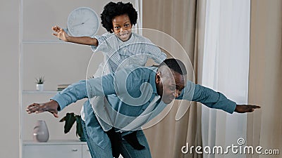 Mature african american grandpa plays with little granddaughter joyful kid pretends to be flying on plane sitting on Stock Photo