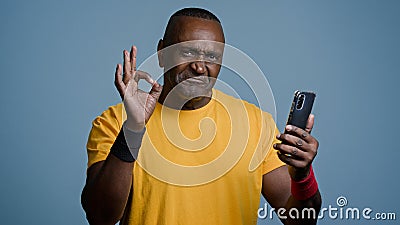 Mature african athletic man stands in studio gray background looking phone screen sportive male athlete trainer browsing Stock Photo