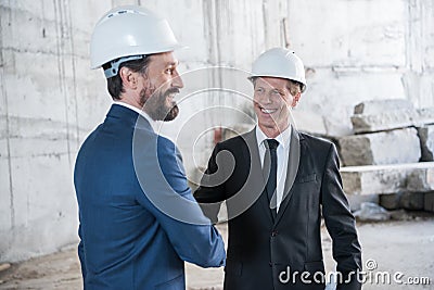 Mature architects in helmets shaking hands and smiling Stock Photo