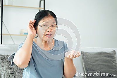 Mature Asian deaf disabled woman having hearing problems holds his hand over the ear, listens carefully, hard of hearing Stock Photo