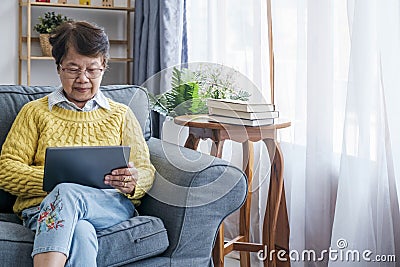 Mature Asian Woman Using Digital Tablet Sitting At Home Stock Photo