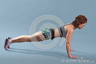 Mature athletic redhead woman doing fitness exercises, gray studio background Stock Photo