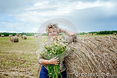 Mature beautiful woman with a bouquet of wild flowers on a mown wheat field. Active recreation, perfect maturity Stock Photo
