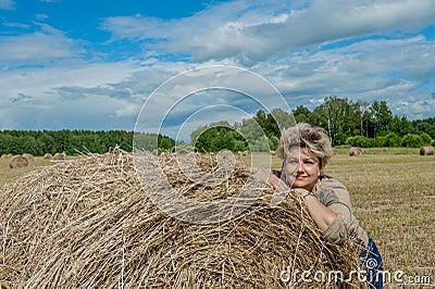 Mature beautiful woman with a bouquet of wild flowers on a mown wheat field. Active recreation, perfect maturity Stock Photo