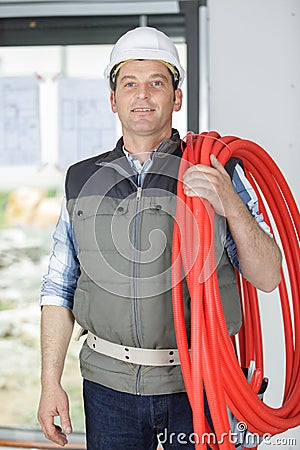 mature builder holding red flexible pipe Stock Photo
