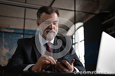 Mature business man in formal clothing using mobile phone. Serious businessman using smartphone and laptop at work Stock Photo